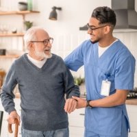 A male caregiver assisting an elderly man to stand