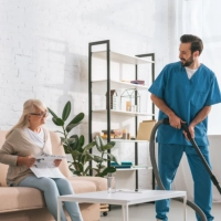 A male caregiver cleaning the room of an elderly woman