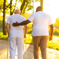 A male assisting an elderly man to walk outside