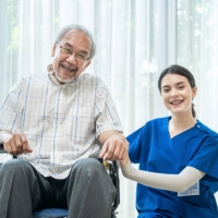 An elderly man sitting on a wheelchair and a female caregiver assisting him