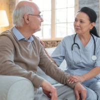 Asian adorable doctor wearing uniform while staring at senior man who sitting next to her