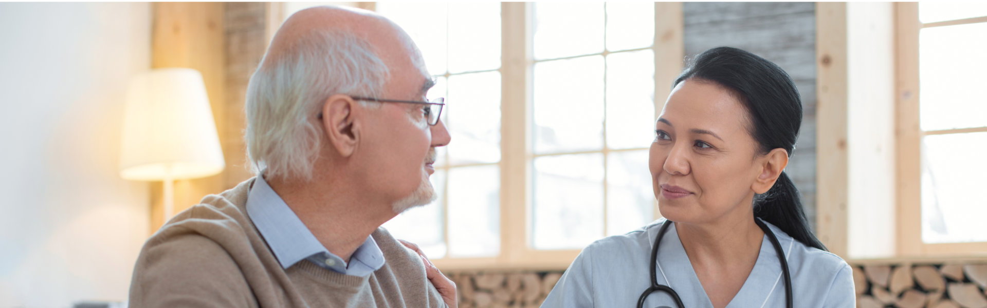 Asian adorable doctor wearing uniform while staring at senior man who sitting next to her