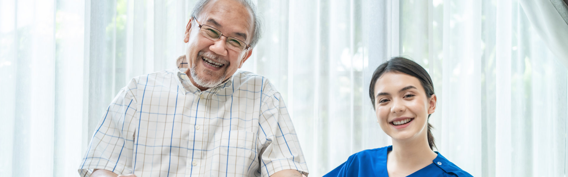 An elderly man sitting on a wheelchair and a female caregiver assisting him